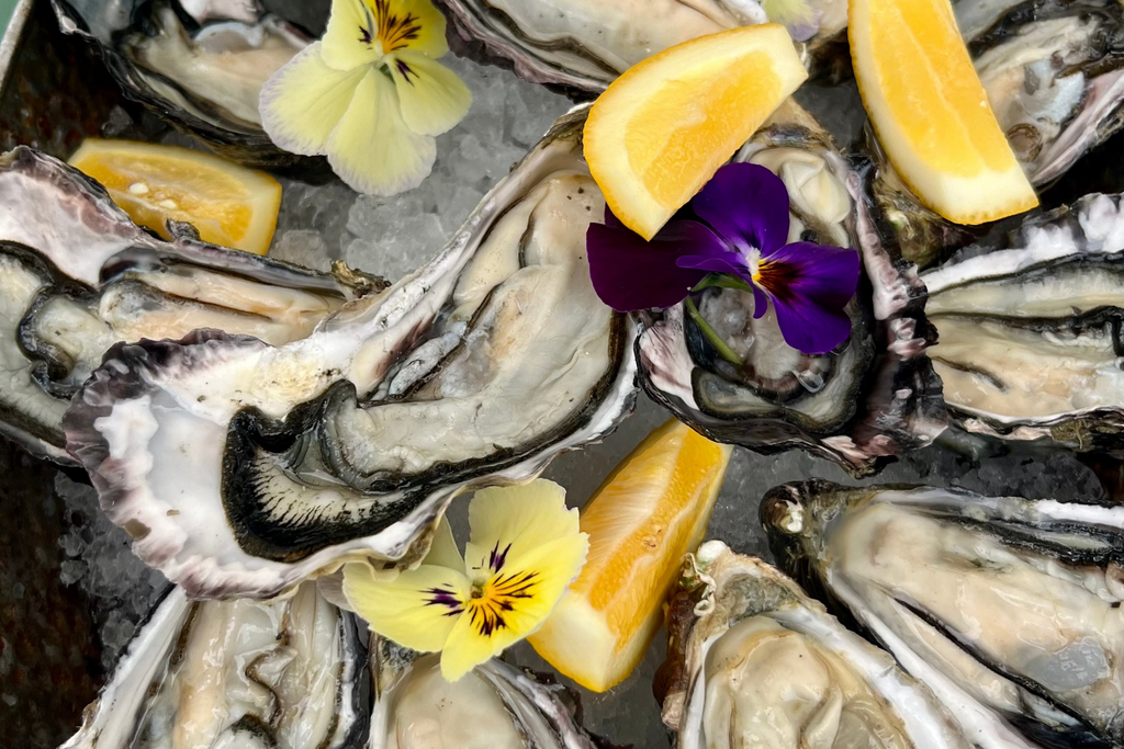 Raw oysters on a bed of lemon wedges and edible flowers on a dark surface